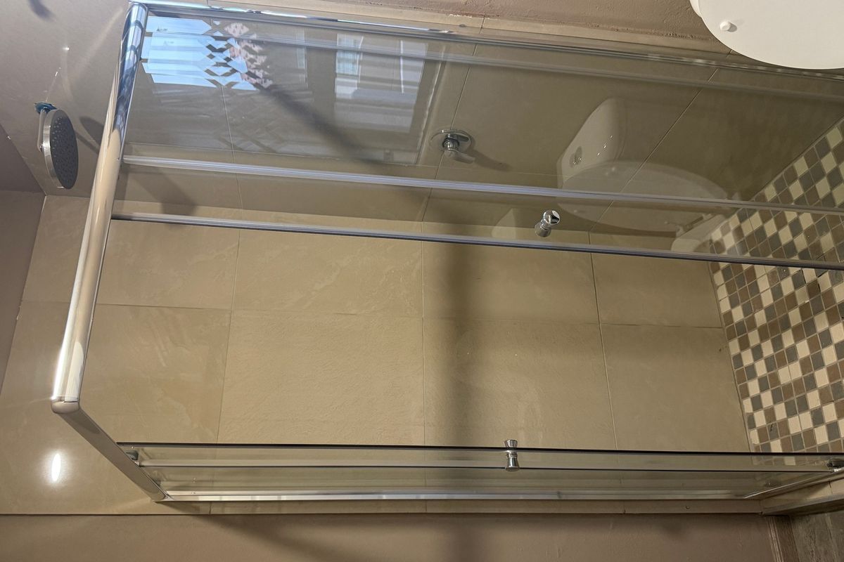 A bathroom featuring a glass shower enclosure, wall-mounted shower head, and a toilet with mosaic floor tiling.