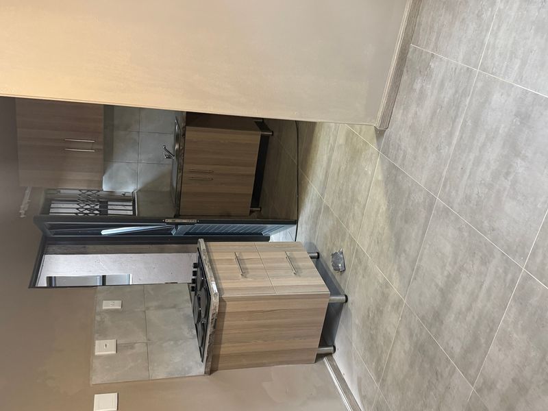 A compact kitchen area featuring built-in cabinetry, a gas hob, and tiled flooring, currently awaiting final finishing touches.