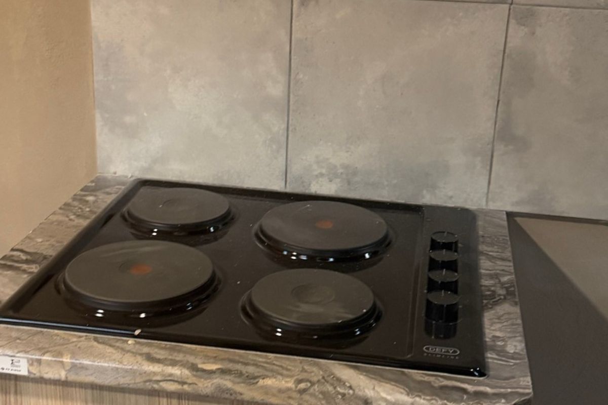 A close-up view of a four-plate electric hob set into a stone-patterned countertop with a neutral tiled backsplash.