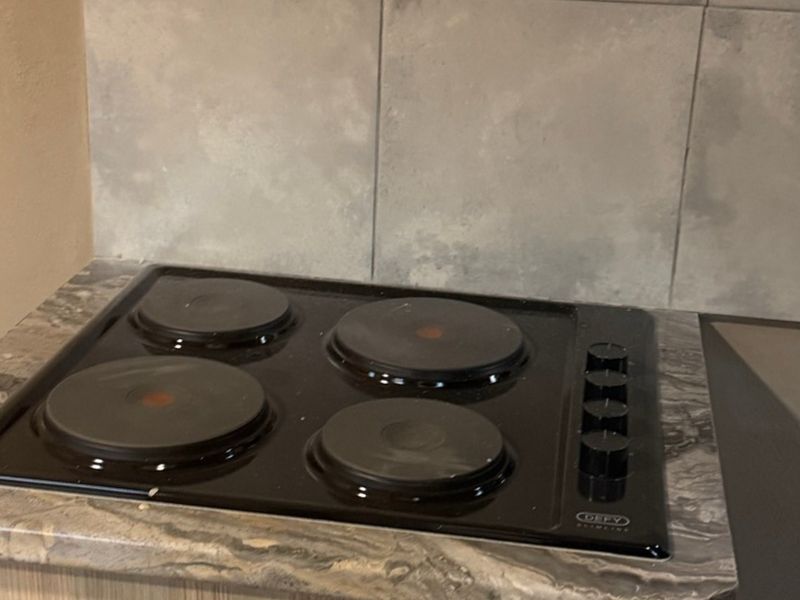A close-up view of a four-plate electric hob set into a stone-patterned countertop with a neutral tiled backsplash.