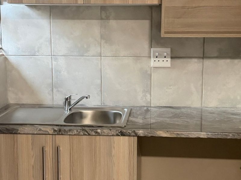 A compact kitchen area featuring a stainless steel sink, marble-effect laminate countertop, light wood-finish cabinetry, and a neutral tiled backsplash.