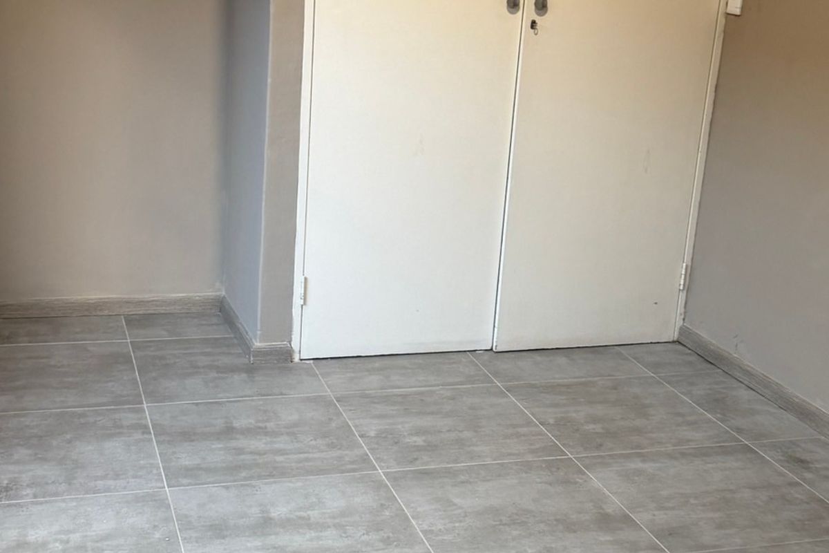 An empty bedroom featuring neutral wall paint, modern grey tiled flooring, and a built-in cupboard with double doors.