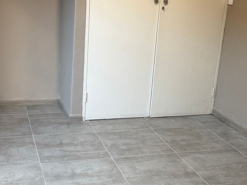 An empty bedroom featuring neutral wall paint, modern grey tiled flooring, and a built-in cupboard with double doors.