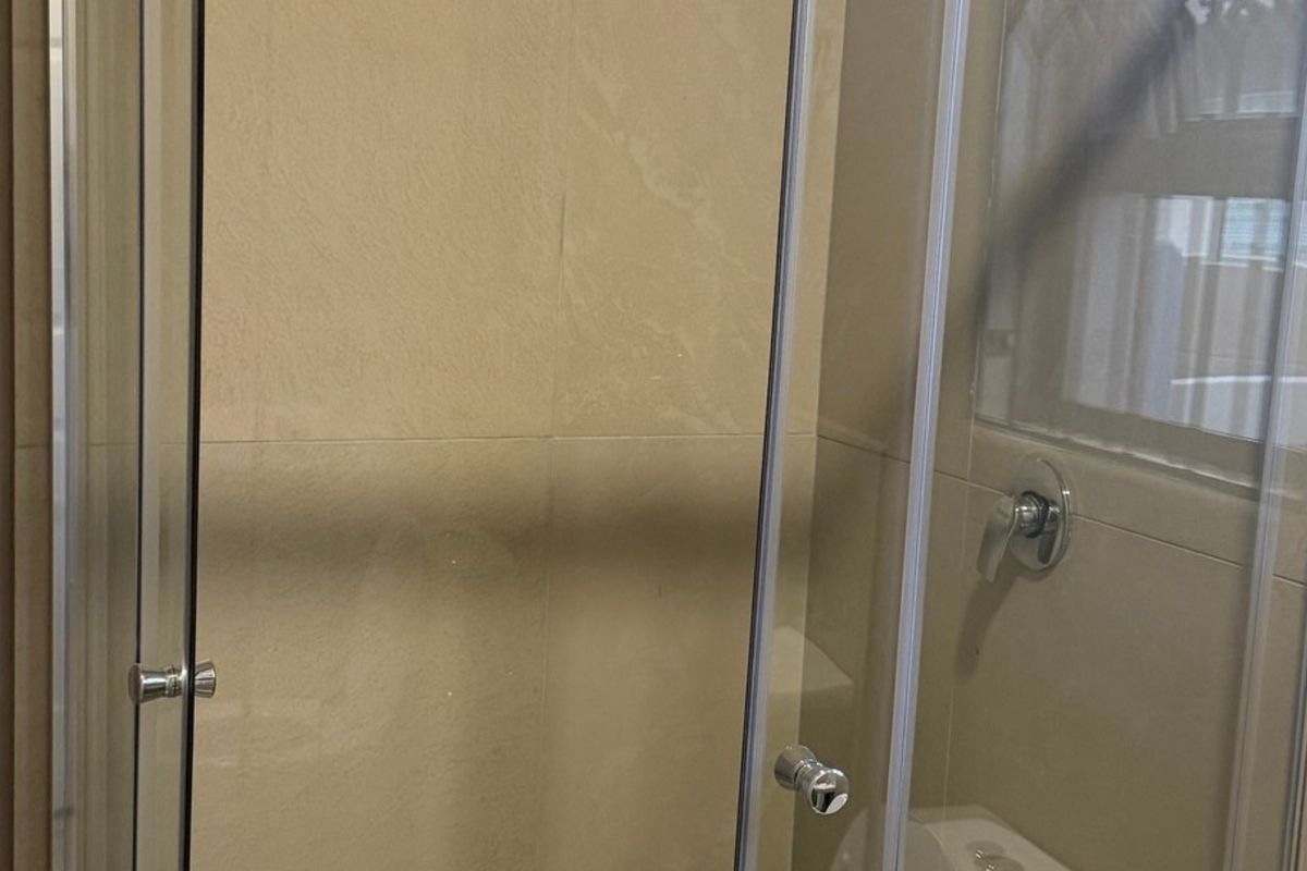 A functional bathroom shower area featuring a glass enclosure and neutral wall tiling.