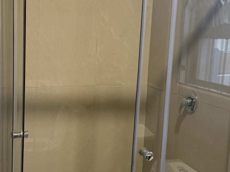 A functional bathroom shower area featuring a glass enclosure and neutral wall tiling.