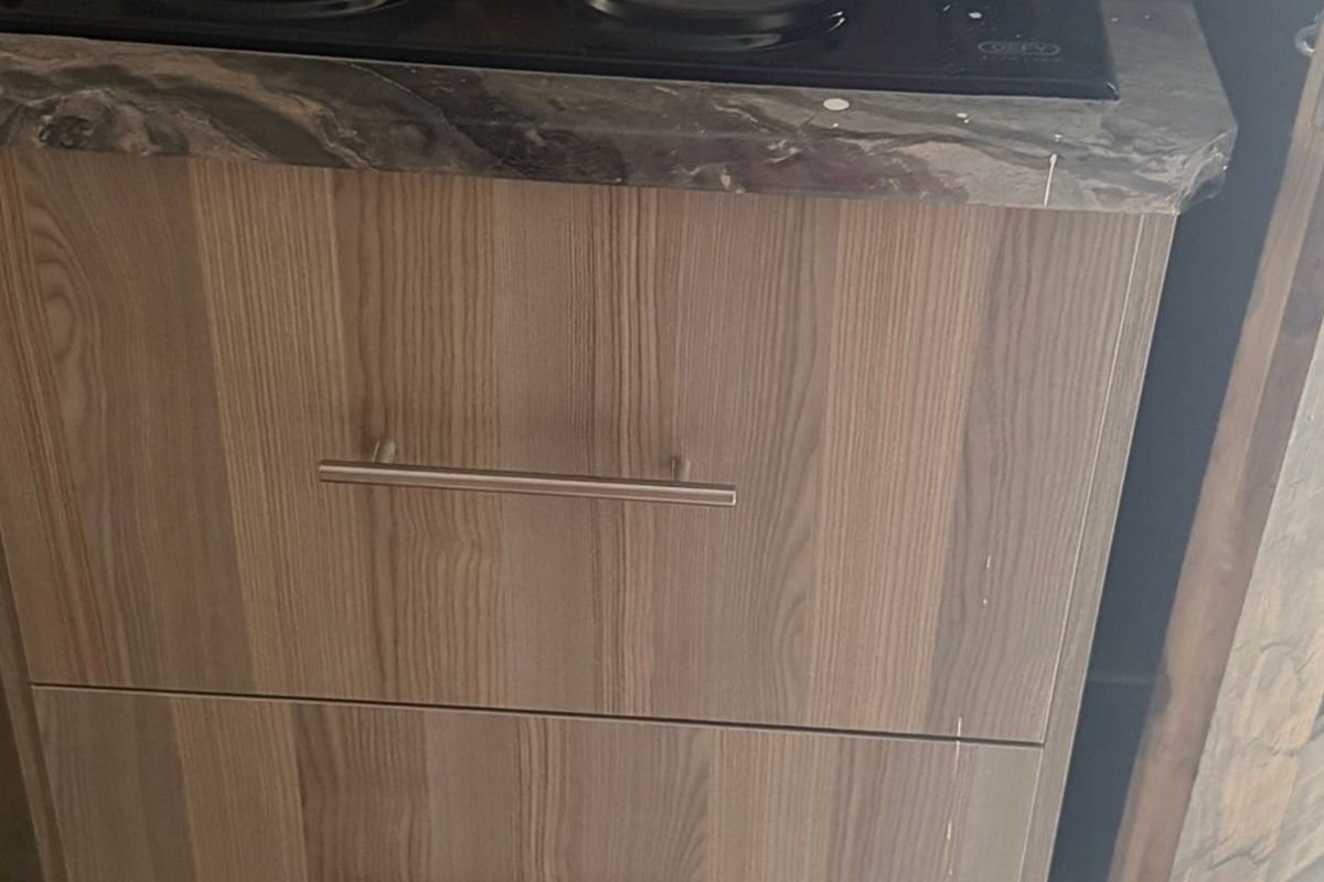 Close-up view of kitchen cabinetry featuring wood-grain finish, laminate countertop, and integrated hob.