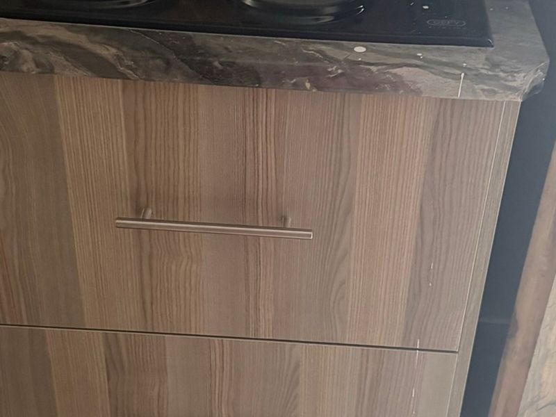 Close-up view of kitchen cabinetry featuring wood-grain finish, laminate countertop, and integrated hob.