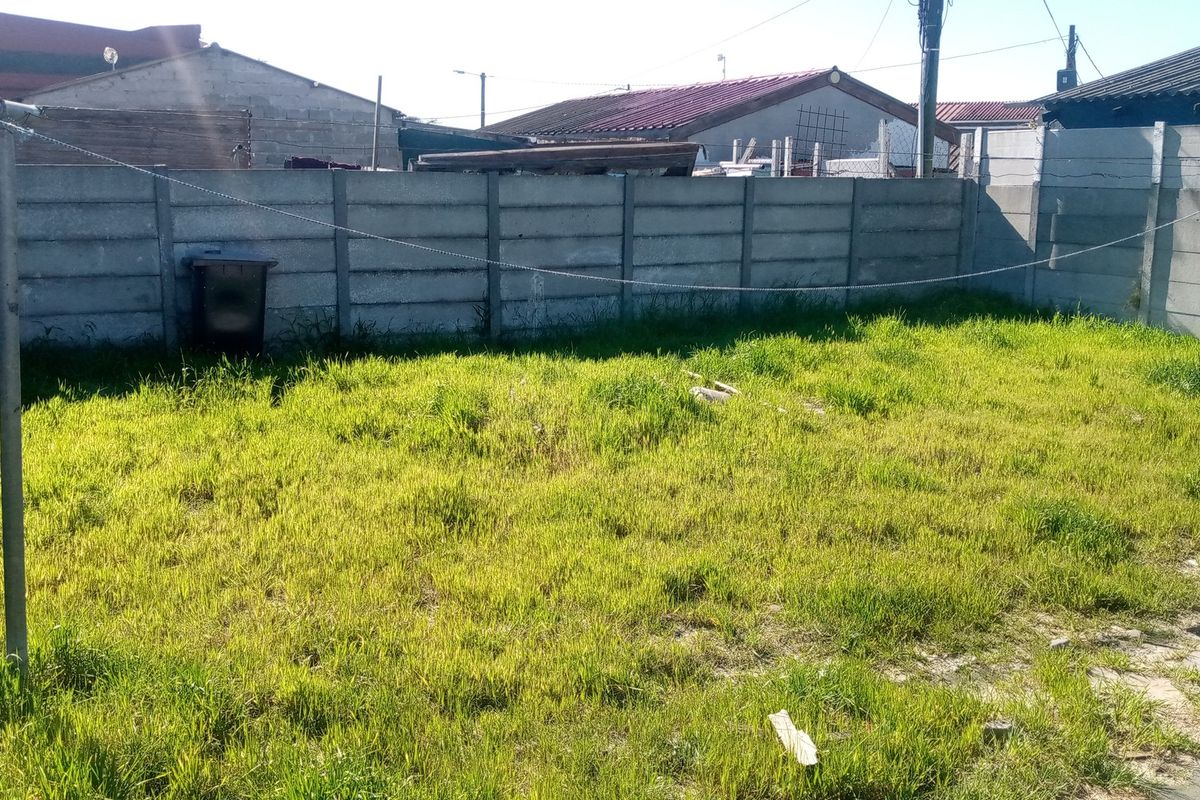 A residential backyard featuring a grass lawn enclosed by a precast concrete boundary wall and equipped with metal washing line poles.