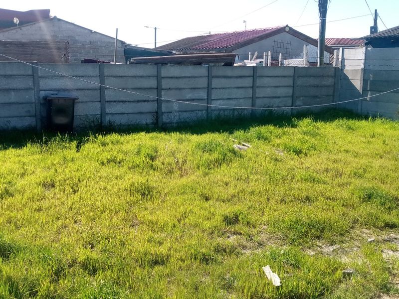A residential backyard featuring a grass lawn enclosed by a precast concrete boundary wall and equipped with metal washing line poles.