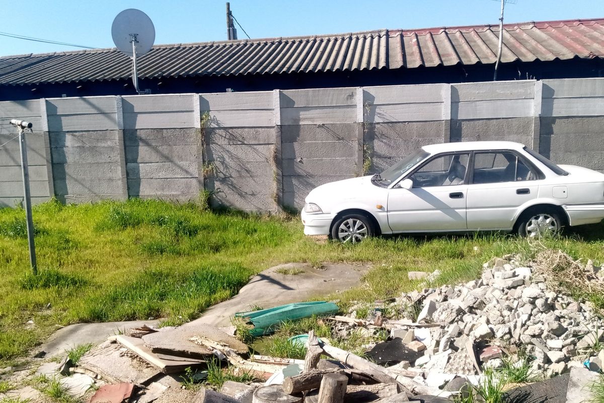 A view of the rear yard featuring a precast concrete boundary wall and significant debris accumulation on the ground.