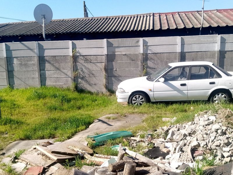 A view of the rear yard featuring a precast concrete boundary wall and significant debris accumulation on the ground.