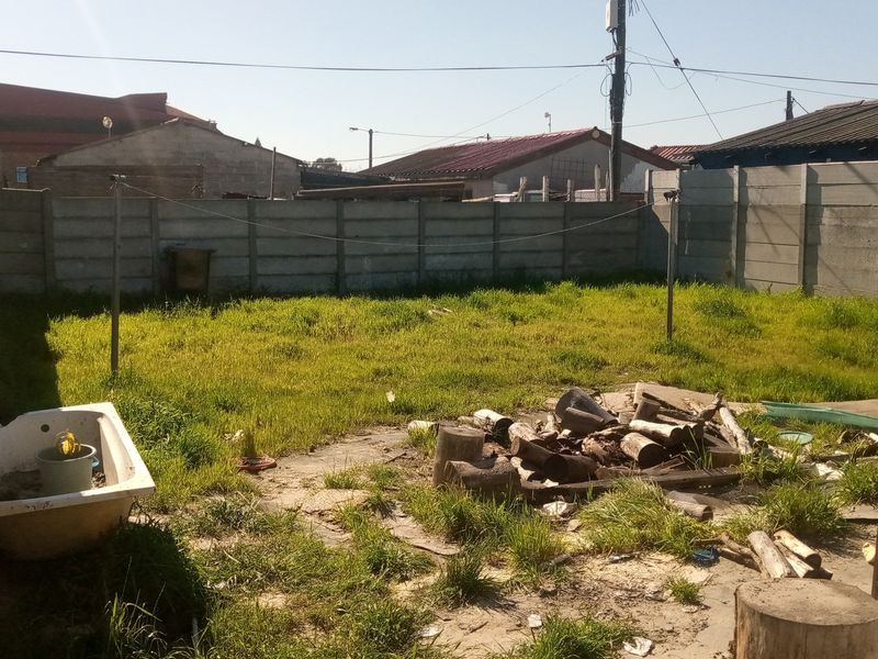 A residential backyard enclosed by precast concrete boundary walls, featuring an open grass area and overhead utility lines.