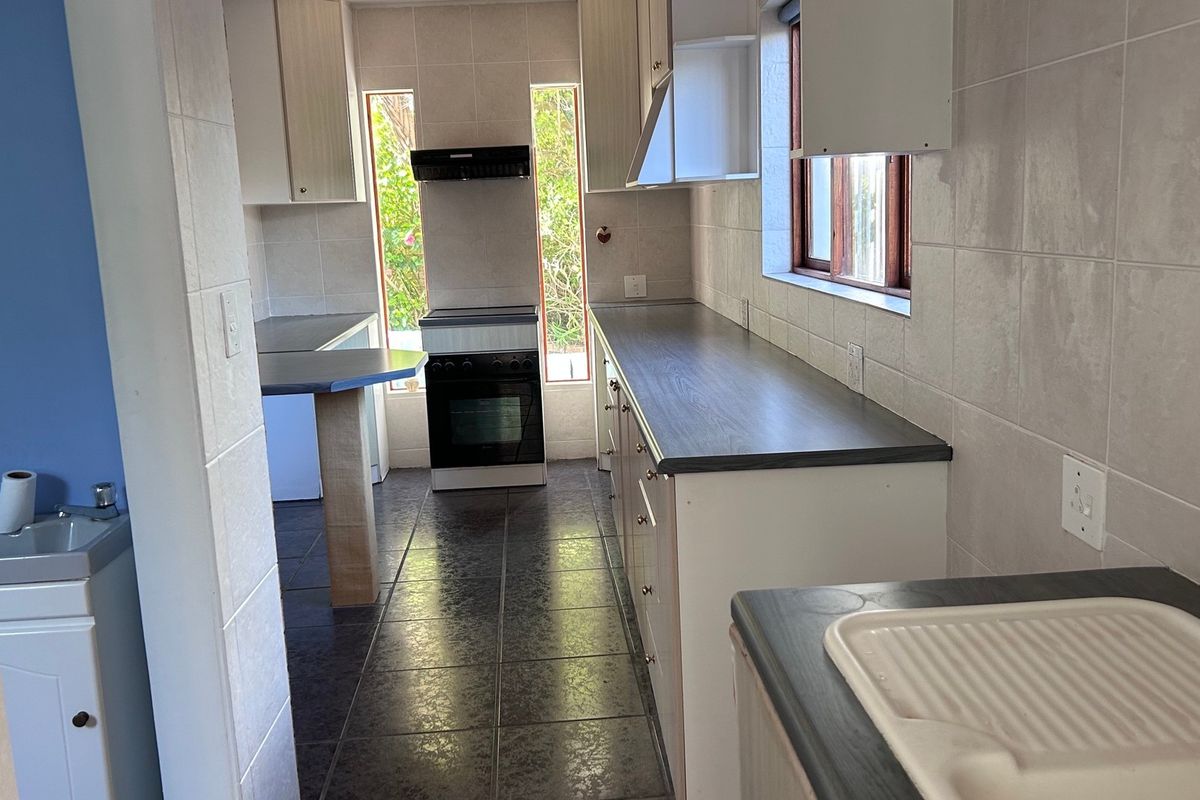 A functional kitchen featuring tiled surfaces, laminate countertops, and a freestanding stove, currently vacant and ready for cosmetic updates.