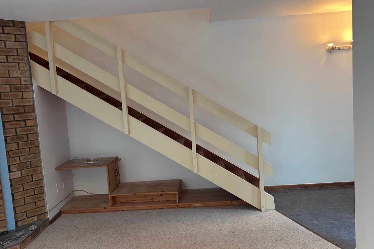 An open living area featuring a staircase, brick fireplace surround, and a mix of carpet and tile flooring.