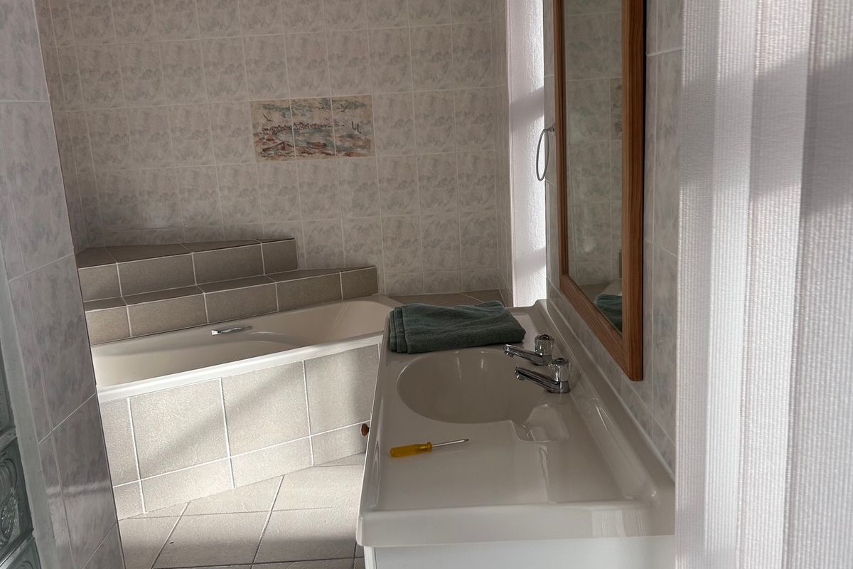 A functional bathroom featuring a built-in tiled bathtub, a vanity basin with a wall mirror, and decorative glass block windows.