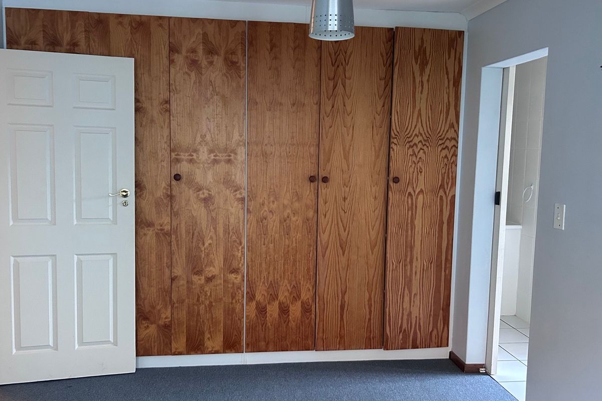 A bedroom featuring built-in wooden cupboards, carpeted flooring, and access to an adjoining bathroom.