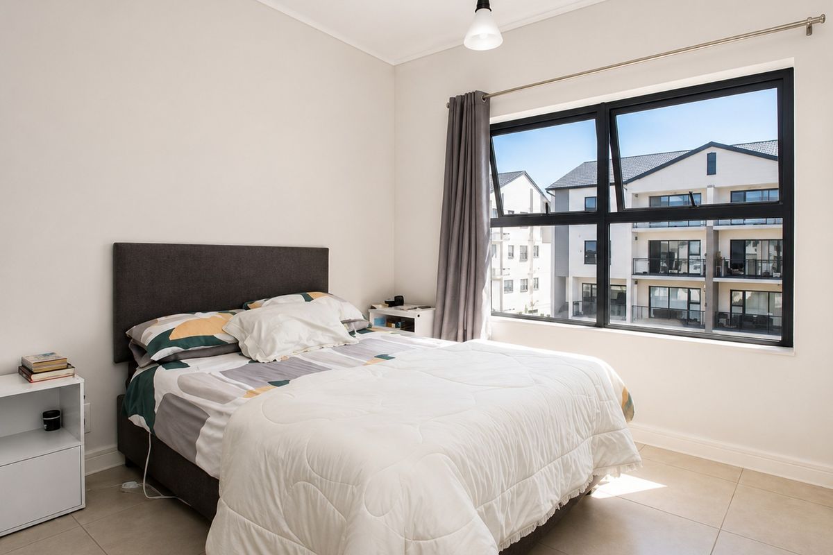 A bright and modern bedroom featuring neutral tiled flooring, a large window with black aluminium frames, and a built-in wardrobe.