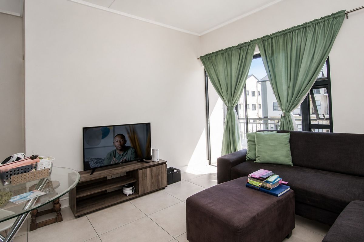 A bright living room featuring neutral tiled flooring and a sliding glass door providing access to a balcony.