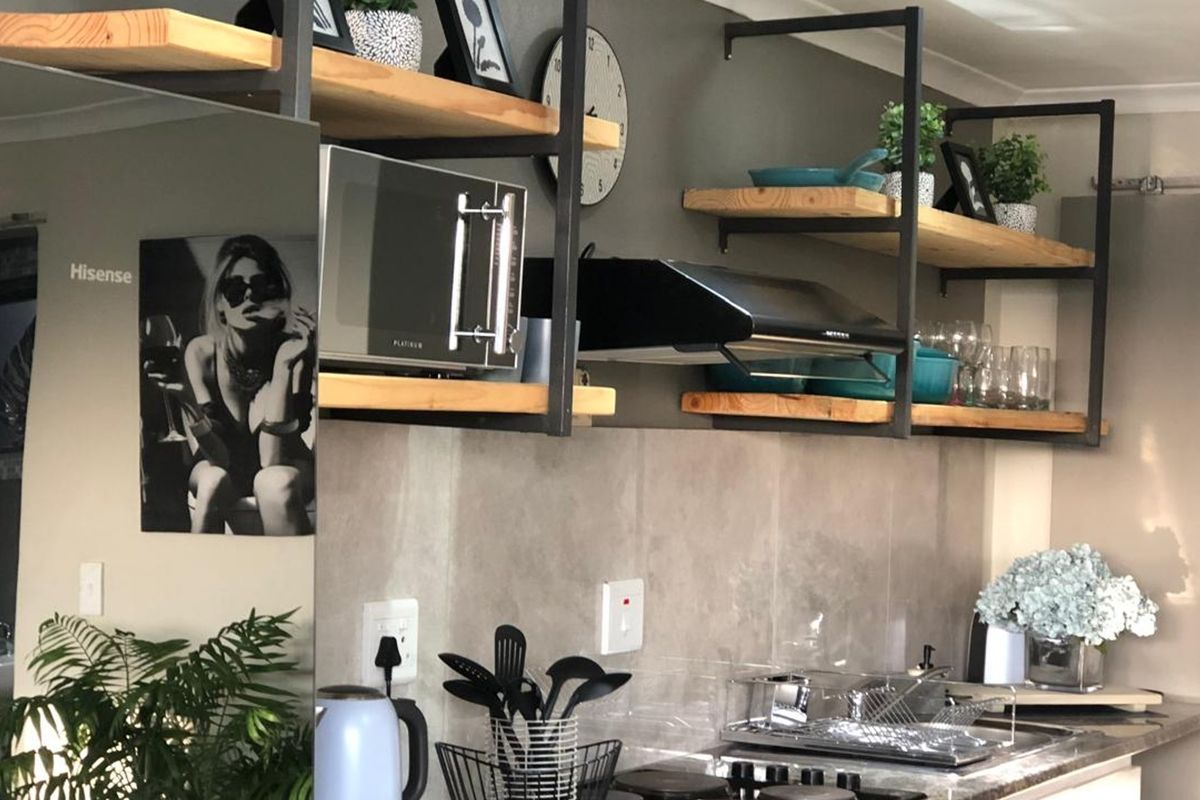 A modern kitchen area featuring industrial-style open shelving, a built-in extractor fan, and a tiled splashback with integrated electrical outlets.