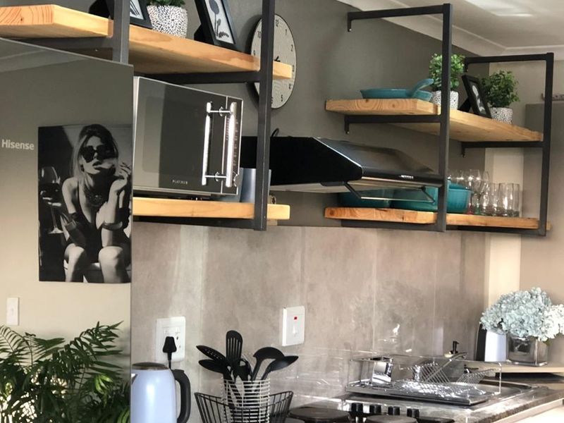 A modern kitchen area featuring industrial-style open shelving, a built-in extractor fan, and a tiled splashback with integrated electrical outlets.