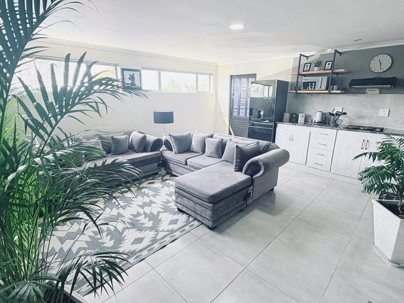 Modern open-plan living area featuring a contemporary kitchen with built-in cabinetry, open shelving, and sleek tiled flooring throughout the space.