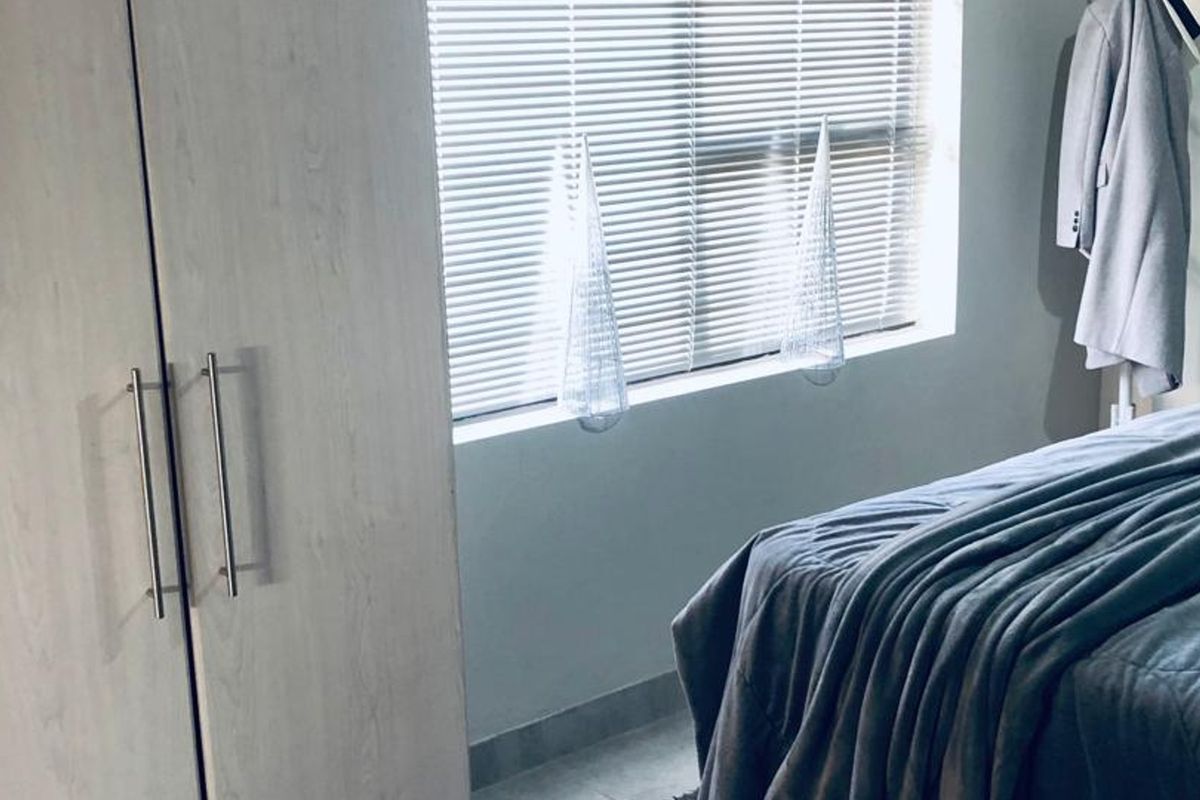 A bedroom featuring a built-in wardrobe with light wood-grain finish and window fitted with venetian blinds.