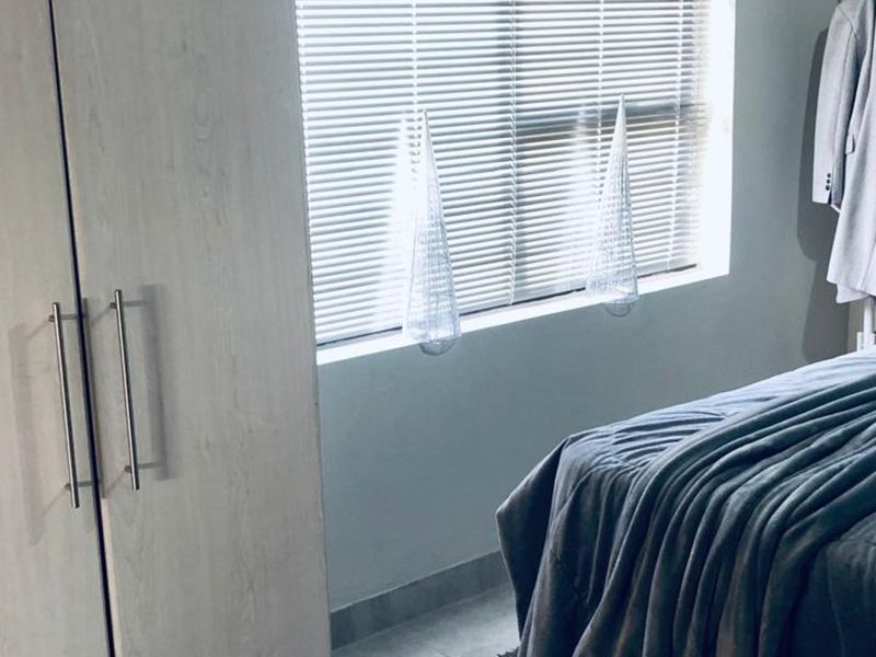 A bedroom featuring a built-in wardrobe with light wood-grain finish and window fitted with venetian blinds.