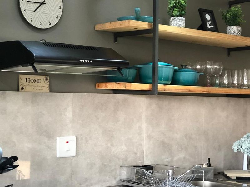 A modern kitchen area featuring a black extractor fan, open timber shelving with metal frames, and neutral grey tiled backsplash.