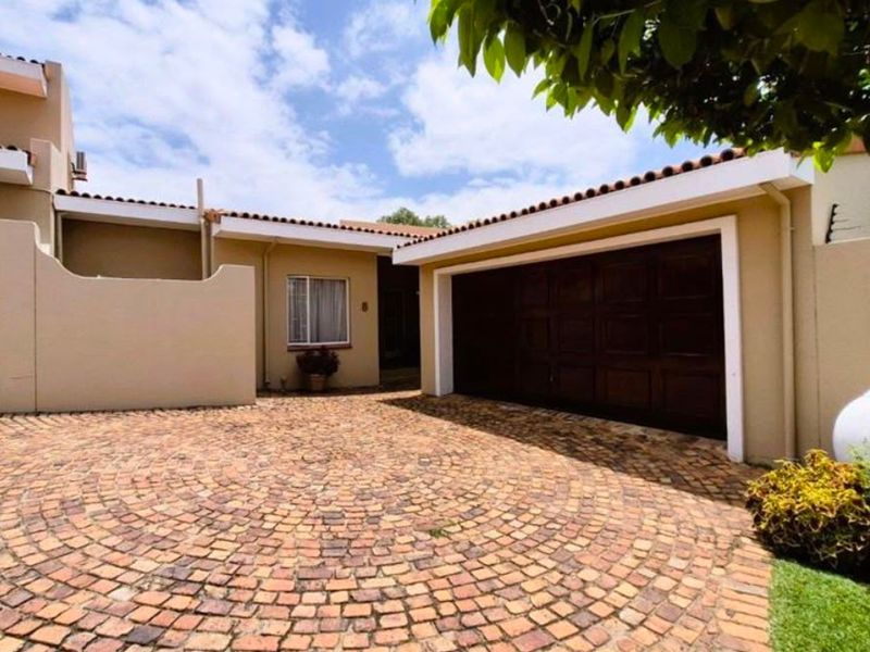 Front exterior view of the townhouse featuring a circular cobblestone driveway, double garage, and secure boundary wall with a timber gate.