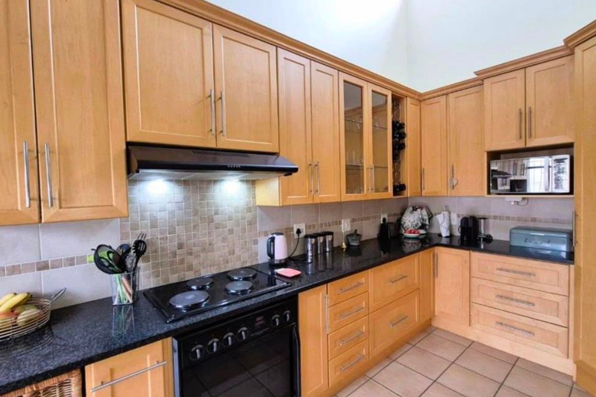 A functional kitchen featuring light wood cabinetry, granite countertops, a tiled backsplash, and integrated appliances including an oven, hob, and microwave.