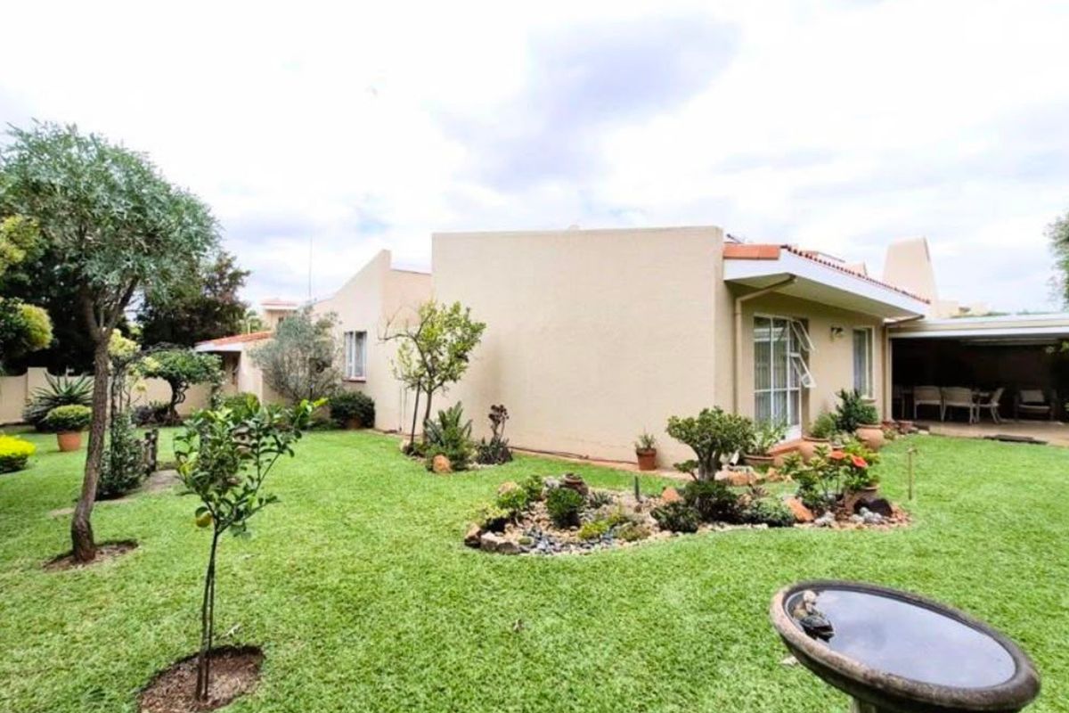 A well-maintained rear exterior view of the townhouse featuring a spacious landscaped garden and a covered patio area.