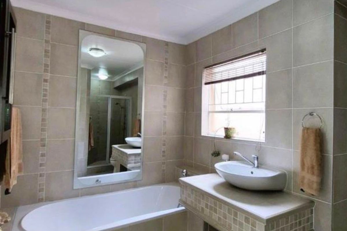 A well-maintained bathroom featuring a built-in bathtub, a modern vessel sink on a tiled vanity, and neutral wall tiling.
