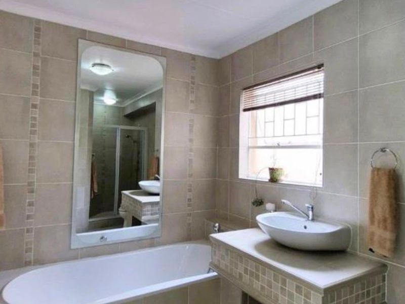 A well-maintained bathroom featuring a built-in bathtub, a modern vessel sink on a tiled vanity, and neutral wall tiling.