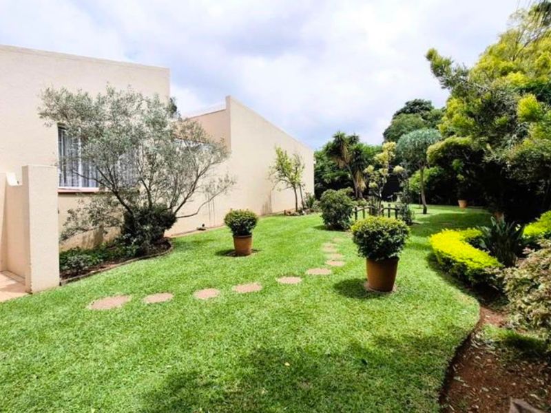 A well-maintained rear garden featuring a lush lawn, landscaped borders, and a paved patio area adjacent to the townhouse structure.