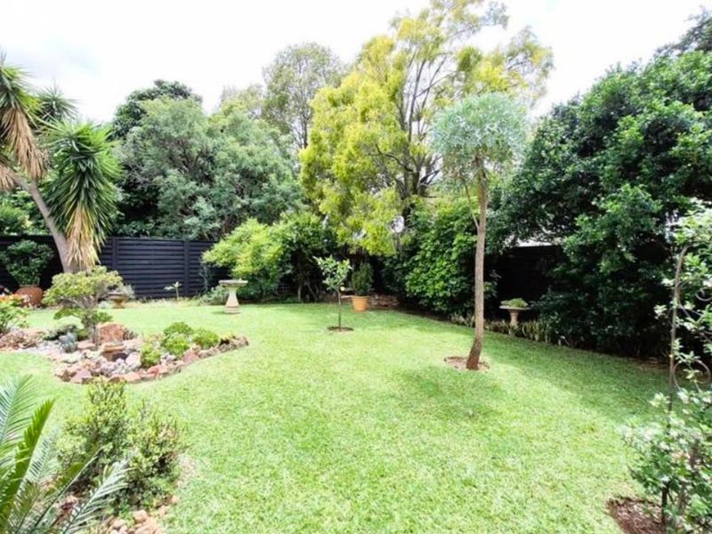 A well-maintained private garden featuring a lush lawn, established trees, and decorative rockery borders enclosed by dark timber fencing.