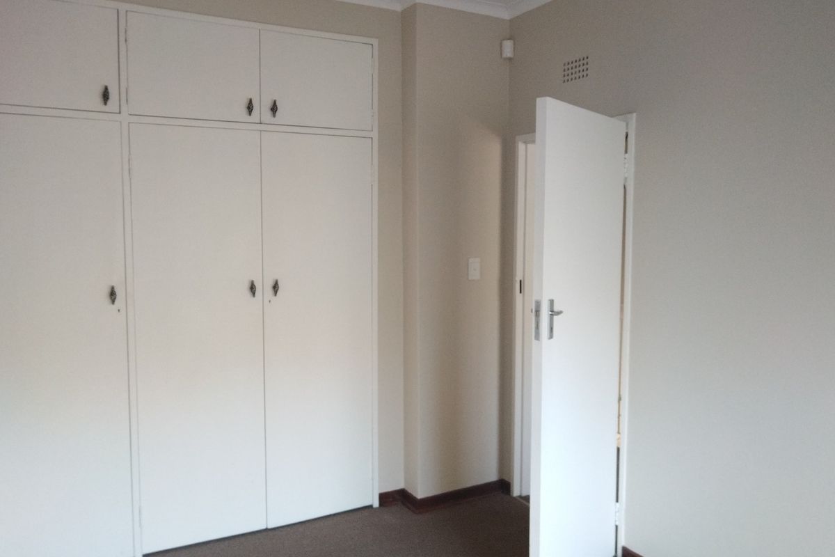 A clean, empty bedroom featuring neutral walls, carpeted flooring, and ample built-in cupboard storage space.