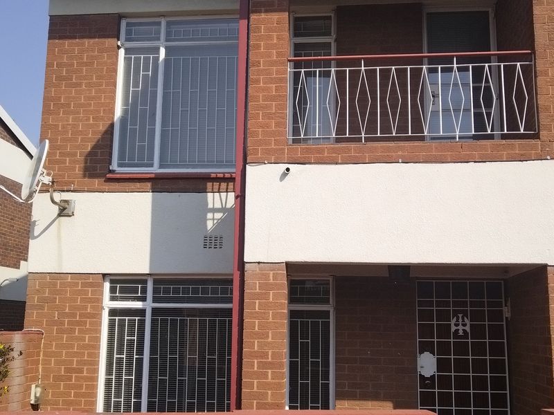 Front elevation of a brick townhouse featuring a balcony with metal railing, security bars on windows, and a satellite dish installation.