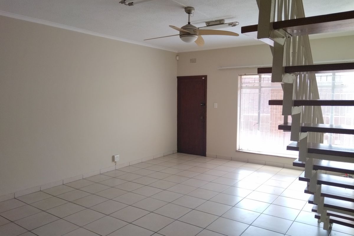 An open-plan living area featuring tiled flooring, a ceiling fan, and a staircase leading to the upper level.