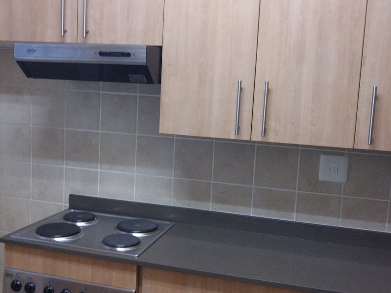 A functional kitchen featuring light wood-finish cabinetry, a dark stone countertop, tiled backsplash, and a built-in electric hob with an extractor fan.