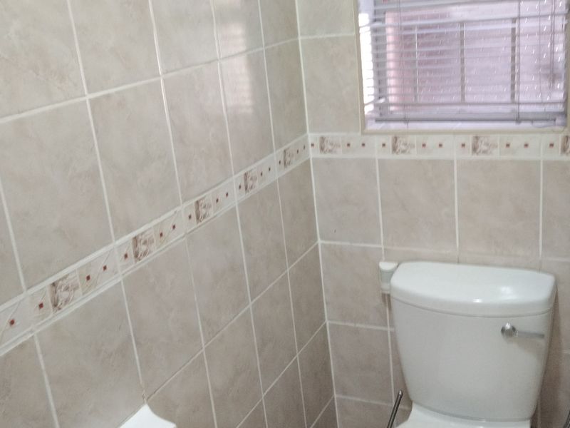 A functional bathroom featuring neutral ceramic wall tiles and a standard toilet with a window blind.
