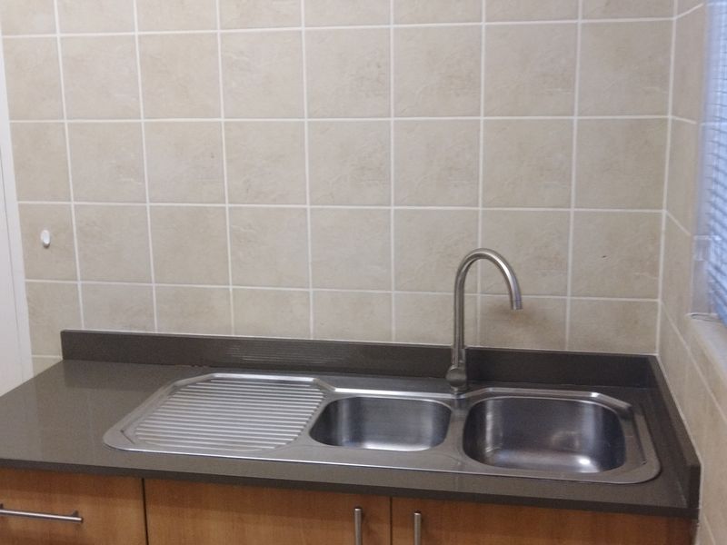 A functional scullery area featuring a stainless steel double sink, gooseneck tap, stone-look countertop, and tiled splashback with timber cabinetry.