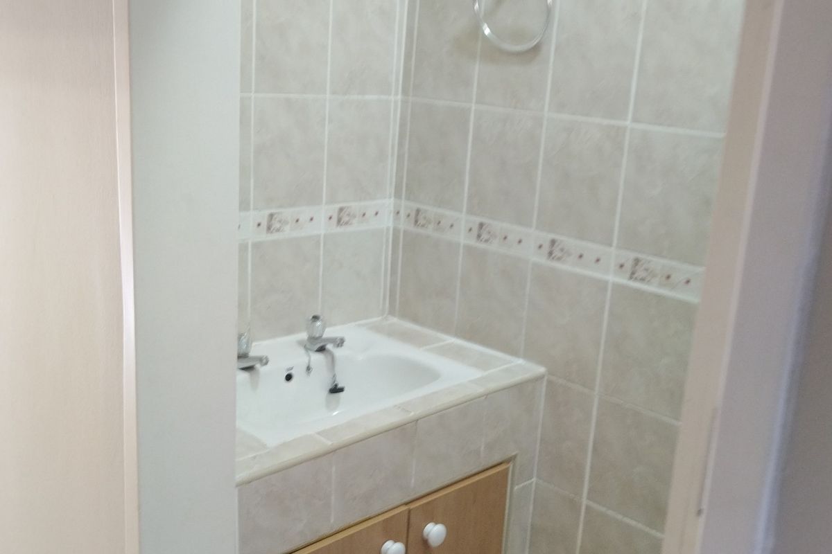 A compact bathroom featuring a built-in vanity cabinet with a ceramic basin and neutral wall tiling.