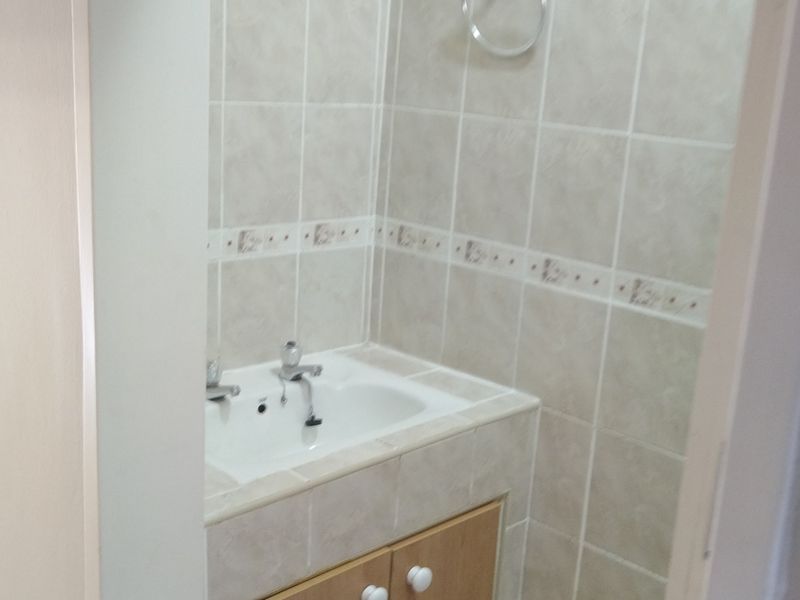 A compact bathroom featuring a built-in vanity cabinet with a ceramic basin and neutral wall tiling.