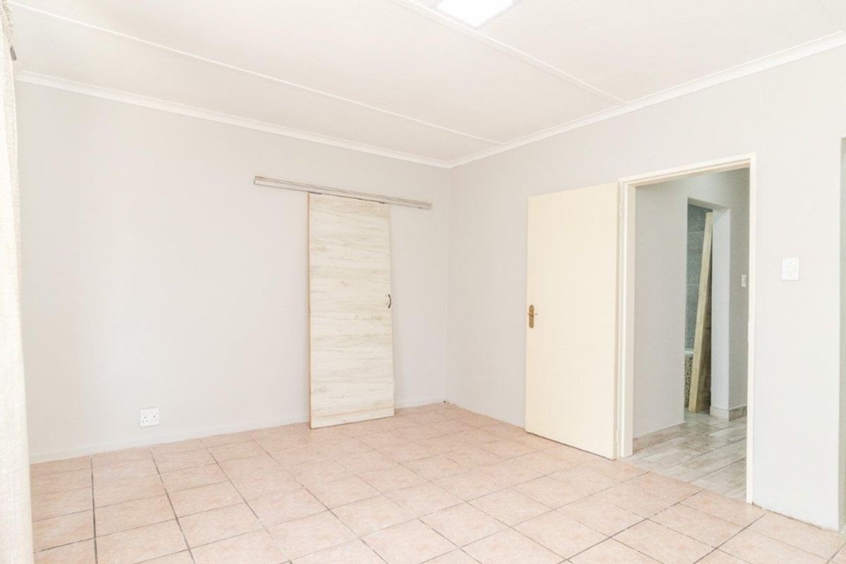 A bright, empty bedroom featuring neutral walls, tiled flooring, and a modern sliding barn door, offering a clean canvas for personalization.