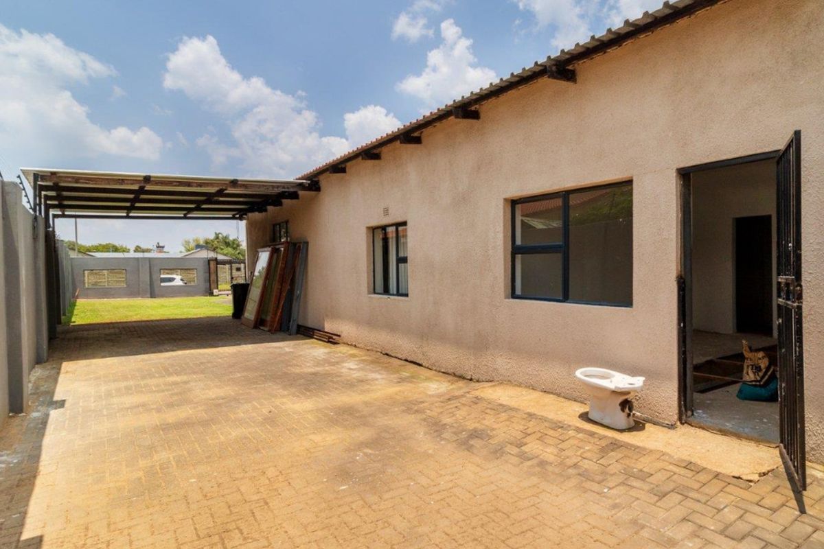 Rear exterior view featuring a paved driveway, carport structure, and boundary wall with electric fencing.