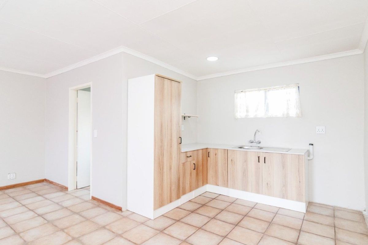 A clean, empty kitchen featuring light wood-look cabinetry, laminate countertops, a stainless steel sink, and neutral tiled flooring.
