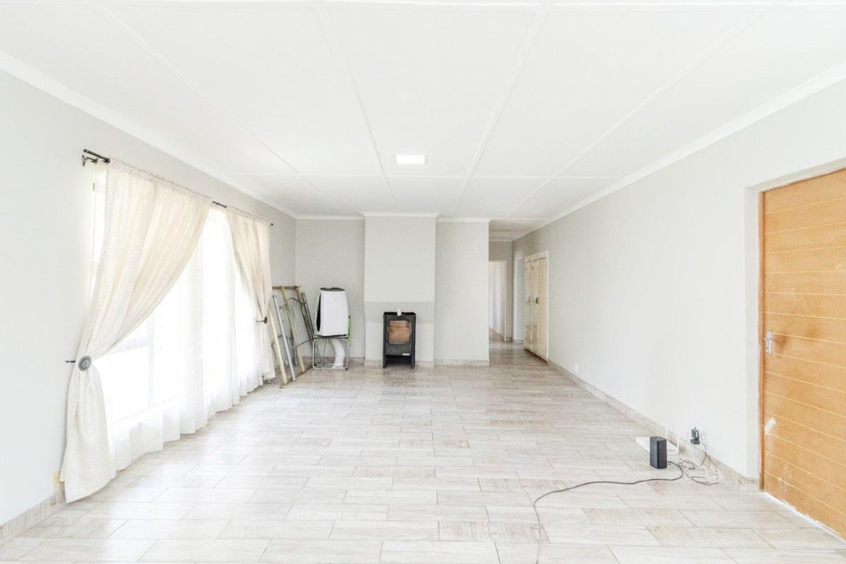 Spacious living area featuring light-toned tiled flooring, a central freestanding fireplace, and neutral wall finishes, offering a bright and versatile open-plan space.