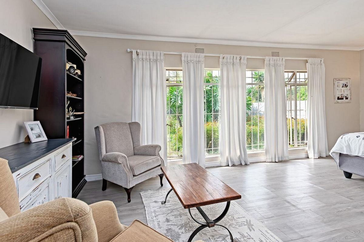 Spacious bedroom featuring light-toned laminate flooring, large windows with security bars, and neutral wall finishes, offering a bright and comfortable living space.