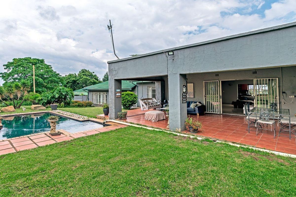 Rear view of the property featuring a covered patio, tiled outdoor area, and a swimming pool set within a landscaped garden.