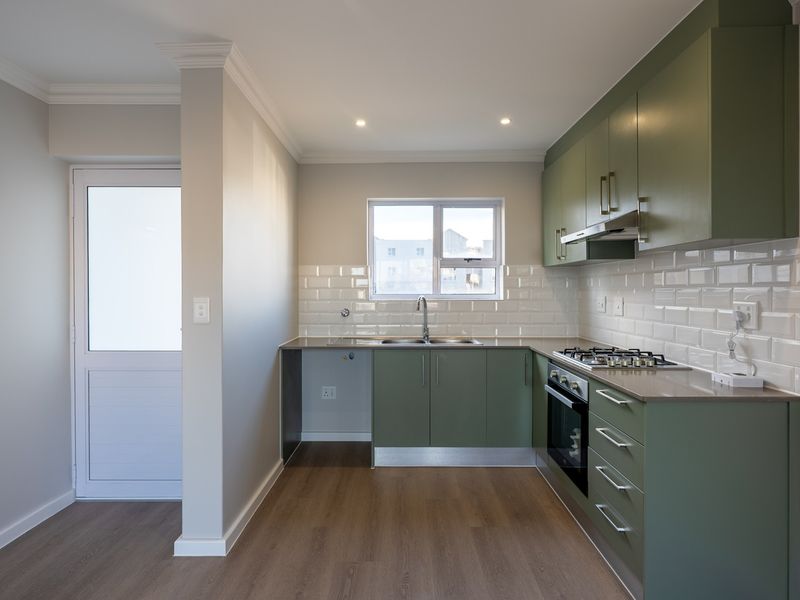 Modern kitchen featuring olive green cabinetry, subway tile backsplash, gas hob, built-in oven, and durable laminate flooring in a clean, well-lit space.